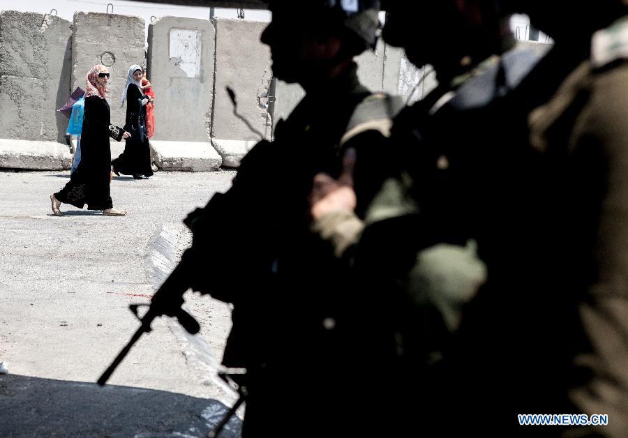 Palestinian women walk by Israeli soldiers to cross the Qalandia checkpoint, located near West Bank City of Ramallah, to go to pray at Al Aqsa mosque in Jerusalem for the 1st Friday of the Holy month of Ramadan on July 20, 2012. (Xinhua/Chen Xu) 