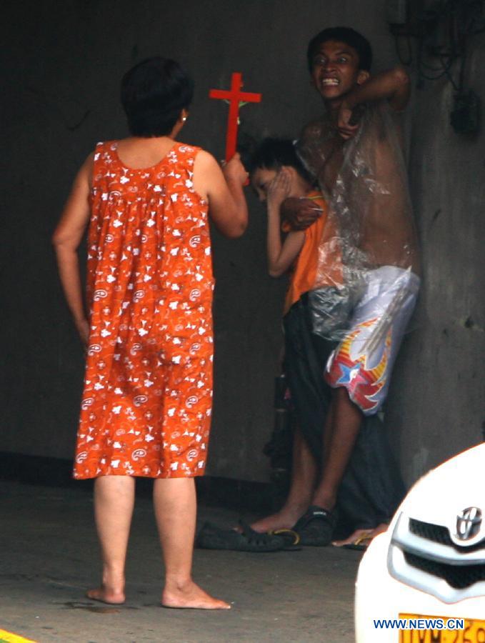 A woman holding a cross talks to her son, who took hostage of a nine-year-old boy with an ice pick in Quezon City, the Philippines, on July 21, 2012. The suspect, Ramir Parparan, was subdued after his mother took advantage of a lull to hold his arms and allow the police to capture him. The boy escaped with minor injuries and was rushed to a nearby hospital after about seven hours of being held hostage. (Xinhua/Rouelle Umali)