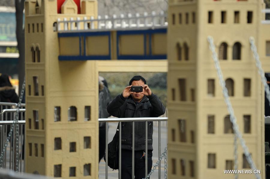 A man takes a photo of a miniature monument of the Tower Bridge on a street in Xi'an, capital of northwest China's Shaanxi Province, Jan. 10, 2013. A collection of miniatures of 10 world cultural heritages are on show here. (Xinhua/Li Yibo)