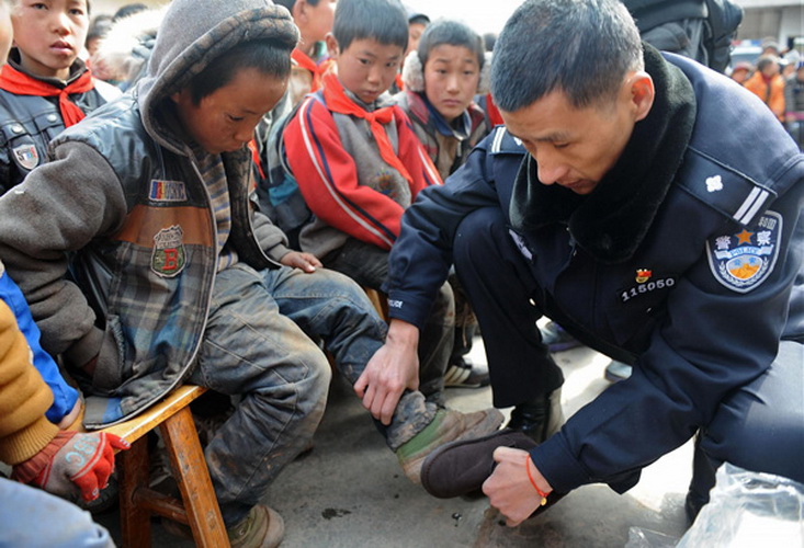 Zhu Dong measures the size of a student's foot before donating shoes at Ersaixiang Primary School, Yuexi county, Southwest China's Sichuan province, on Jan 8, 2013. (Photo/Xinhua)