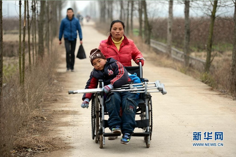 Wu Sulan pushes a wheelchair to send her son Kangle to school on Jan. 8, 2013. The wheelchair was donated by Kangle’s classmates. (Xinhua/Song Zhenping)