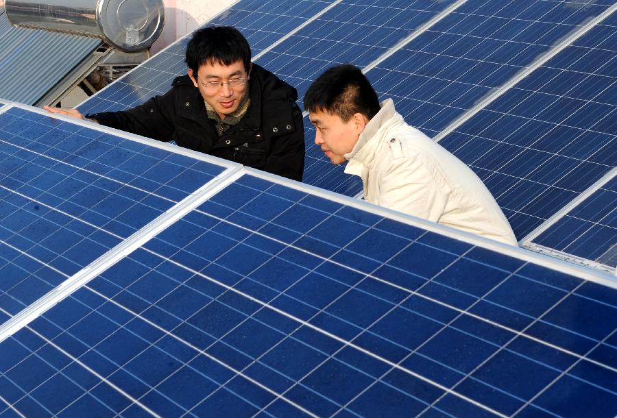 Xu Pengfei (L), China's first individual user of grid-connected photovoltaic (PV) power, introduces PV solar batteries to his friend on the top of his flat building in Qingdao, east China's Shandong Province, Jan. 13, 2013. As Xu's "personal power plant", the eight pieces of PV solar batteries have a total installed capacity of 2 kW, with a grid-connected voltage of 220 V. It not only provides electricity for Xu's family, but also sells surplus electricity to the state grid, which has been the first successful case ever in China. (Xinhua/Li Ziheng) 