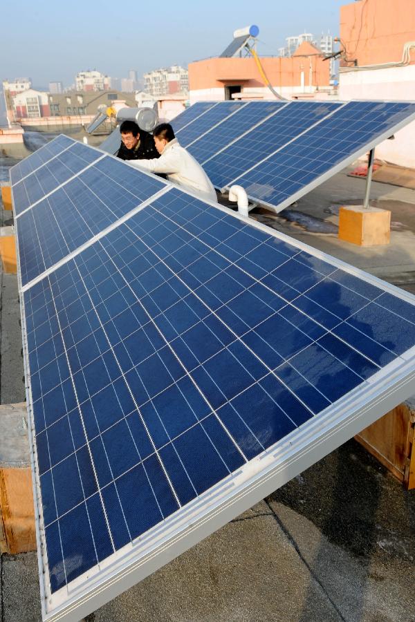 Xu Pengfei (L), China's first individual user of grid-connected photovoltaic (PV) power, introduces PV solar batteries to his friend on the top of his flat building in Qingdao, east China's Shandong Province, Jan. 13, 2013. As Xu's "personal power plant", the eight pieces of PV solar batteries have a total installed capacity of 2 kW, with a grid-connected voltage of 220 V. It not only provides electricity for Xu's family, but also sells surplus electricity to the state grid, which has been the first successful case ever in China. (Xinhua/Li Ziheng) 