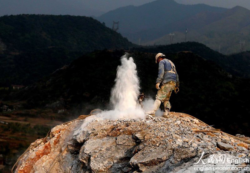 Limestone power erupts 2 meters high from a mine, forcing a worker to stay back in a mountain area in western Zhejiang on Dec. 4, 2012. (Photo/People's Daily Online)