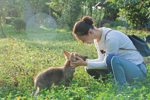 Li Weiyi plays with wolf cub Green on the grass in their early days together. (China Daily)
