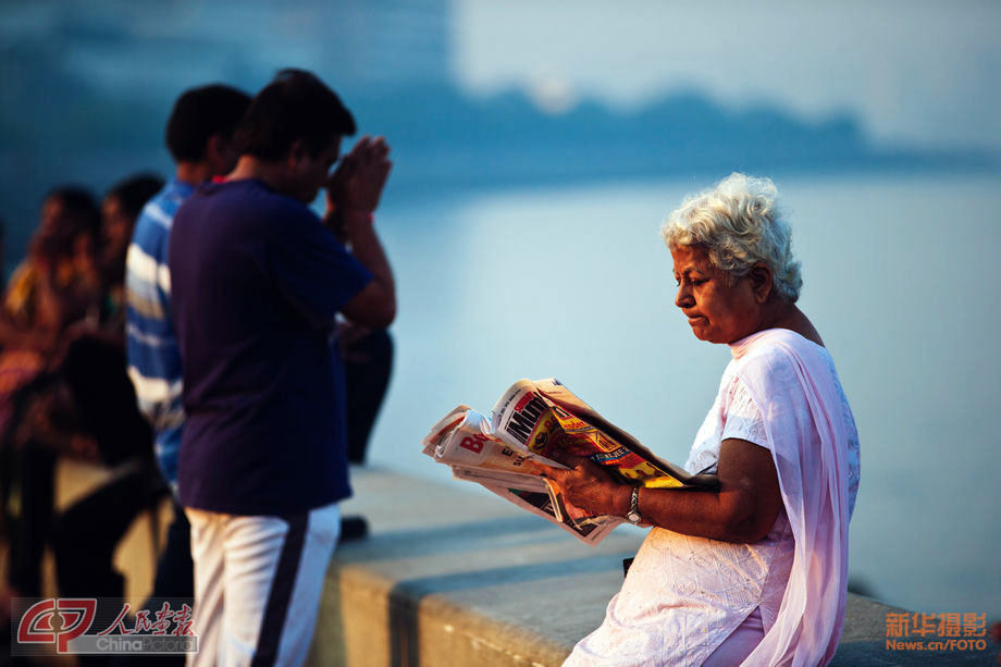 An old woman reads newspapers as others are praying. (Chinapictorial/ Duan Wei)