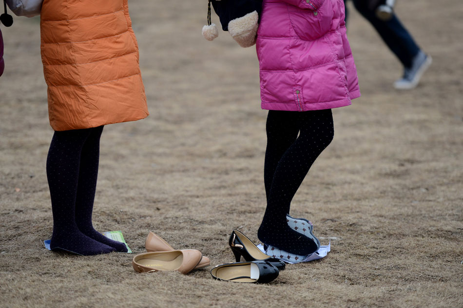 A girl tries to ease the pain on feet caused by wearing high heels and cold weather as she waits outside for an entrance examination for the art college in Anhui province, Jan. 17. (Xinhua/Zhang Rui)