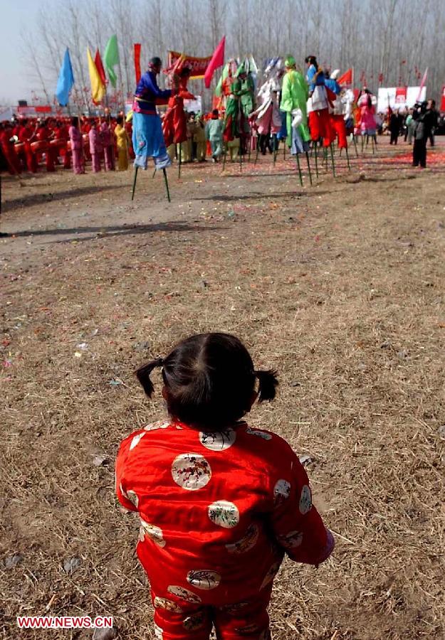 File photo taken on Feb. 17, 2002 shows a little girl watches stilts performance at a temple fair in Zhengzhou, capital of central China's Henan Province. Temple fair in central China area is an important social activity for local people. The ancient temple fairs in central China were ceremonious sacrificial rituals. As time goes by, the focus of temple fair activities has shifted from "gods" to "people". The modern temple fair in central China is a platform of displaying folk culture as well as a channel for commodity circulation. According to statistics from the provincial cultural sector, there are about 35,000 temple fairs each year in Henan. (Xinhua/Wang Song)