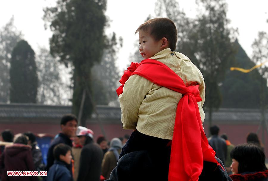 File photo taken on March 9, 2008 shows a boy wearing red silk sits on his family member's shoulders to offer incense at a temple fair in Huaiyang County, central China's Henan Province. Temple fair in central China area is an important social activity for local people. The ancient temple fairs in central China were ceremonious sacrificial rituals. As time goes by, the focus of temple fair activities has shifted from "gods" to "people". The modern temple fair in central China is a platform of displaying folk culture as well as a channel for commodity circulation. According to statistics from the provincial cultural sector, there are about 35,000 temple fairs each year in Henan. (Xinhua/Wang Song)