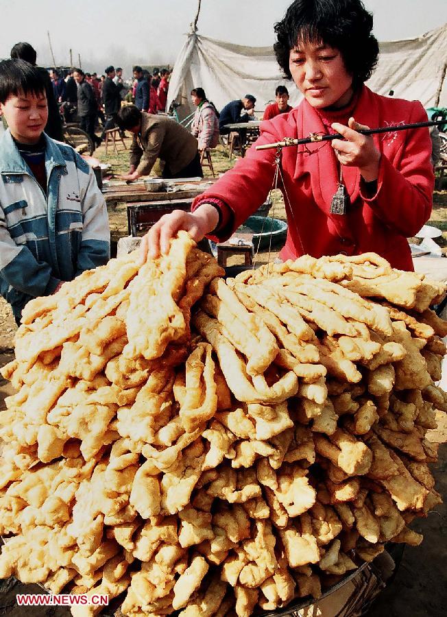 File photo taken on March 19, 2004 shows a woman sells local snacks at a temple fair in Ruyang County, central China's Henan Province. Temple fair in central China area is an important social activity for local people. The ancient temple fairs in central China were ceremonious sacrificial rituals. As time goes by, the focus of temple fair activities has shifted from "gods" to "people". The modern temple fair in central China is a platform of displaying folk culture as well as a channel for commodity circulation. According to statistics from the provincial cultural sector, there are about 35,000 temple fairs each year in Henan. (Xinhua/Wang Song)