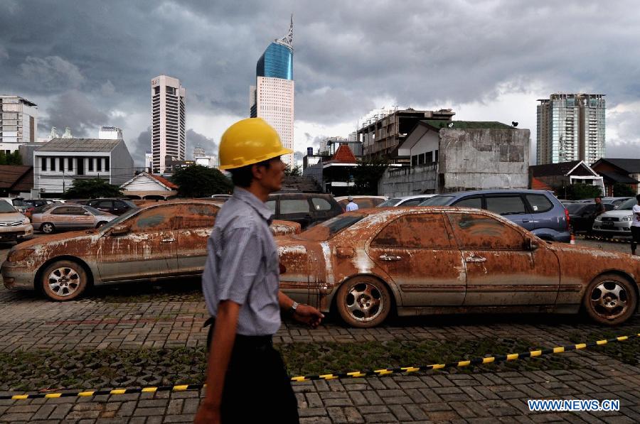 A man walks past some cars covered with mud from a flooded basement in Jakarta, Indoensia, Jan. 23, 2013. (Xinhua/Agung Kuncahya B.) 