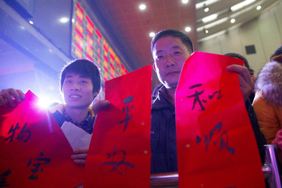 Two passengers show the Spring Festival couplets distributed by volunteers at the station in Hangzhou, capital of east China's Zhejiang Province, Jan. 23, 2013. A group of volunteers visited the train station in Hangzhou, offering the passengers hot ginger beverage, snacks and Spring Festival Couplets. Stations in Hangzhou embraced more passengers ahead of the Spring Festival travel peak. (Xinhua/Cui Xinyu) 