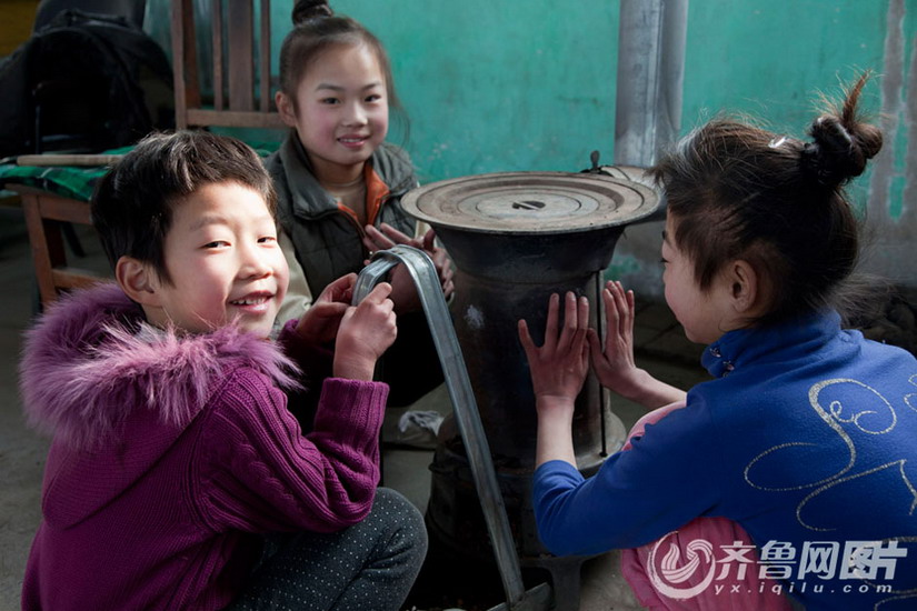 Children gather around a stove to make warm during break time.  (Photo/ Yx.iqilu.com)