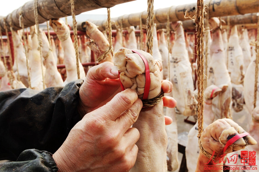 The worker binds the toes of the ham with a rubber band.