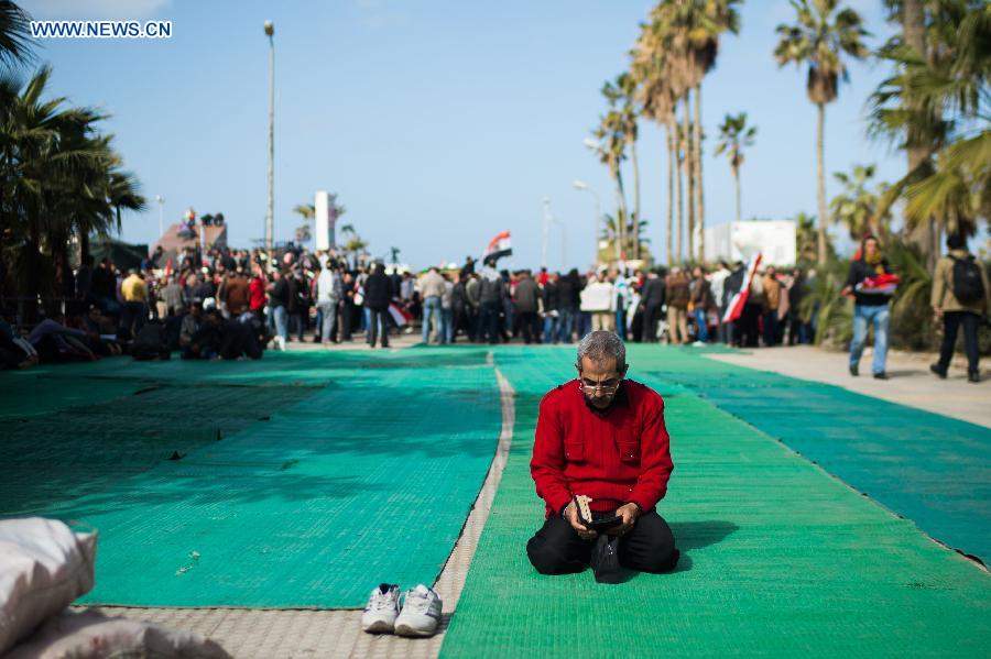 A Egyptian reads the Quran while protestors participate in a rally in front of Al Qaed Ibrahim Mosque in Alexandria, the second biggest city of Egypt, on Jan. 25, 2013, marking the second anniversary of the 2011 unrest that toppled former leader Hosni Mubarak. (Xinhua/Qin Haishi)