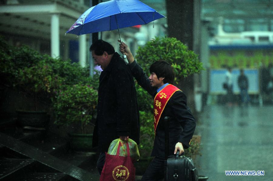 A volunteer holds umbrella for a passenger at the Nanning Railway Station in Nanning, capital of south China's Guangxi Zhuang Autonomous Region, Jan. 26, 2013. As the Spring Festival, which falls on Feb. 10 this year, draws near, lots of people rushed to start their journey home. (Xinhua/Huang Xiaobang)