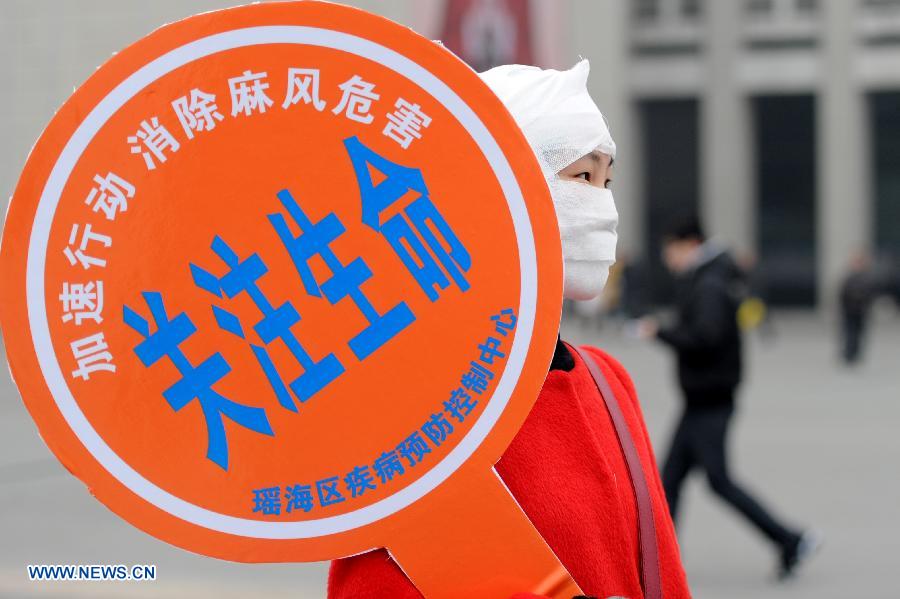 A staff member dressed like a leprosy patient with bandage holds a cardboard written with the slogan of leprosy prevention on the square of the Hefei Railway Station in Hefei, capital of east China's Anhui Province, Jan. 27, 2013. Staff members from a local center for disease control and prevention carried out a campaign to promote leprosy prevention here on Sunday, the 60th World Leprosy Day. (Xinhua/Liu Junxi) 