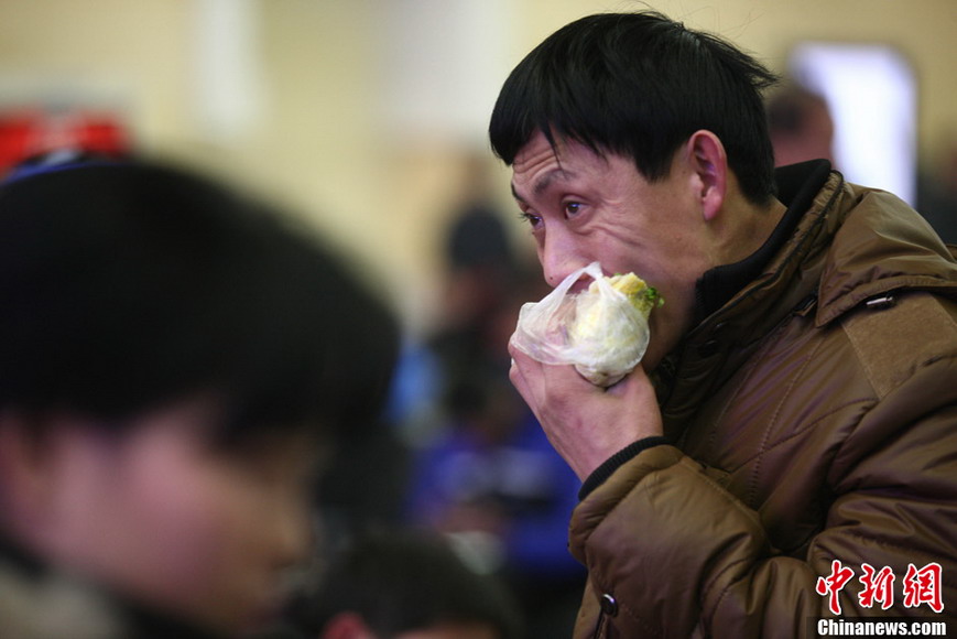 A traveler swallows food to catch the train at Qingdao Railway Station on Jan. 26, 2013. (CNS/XU Chongde)