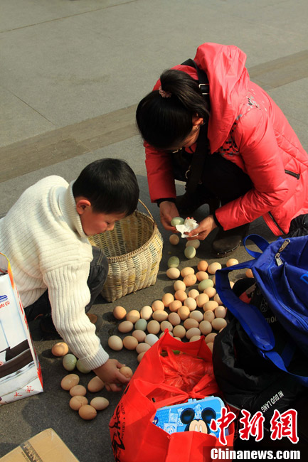 A little traveler and his mother pack and pick up fallen eggs from ground at Hankou Railway Station on Jan. 26, 2013. (CNS/Zhang Chang)