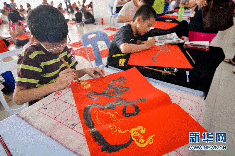 Contestants write down the Chinese character "she", meaning snake, on the piece of red paper with writing brush on Sunday in Selangor, Malaysia. (Xinhua Photo by Zhang Wenzong)