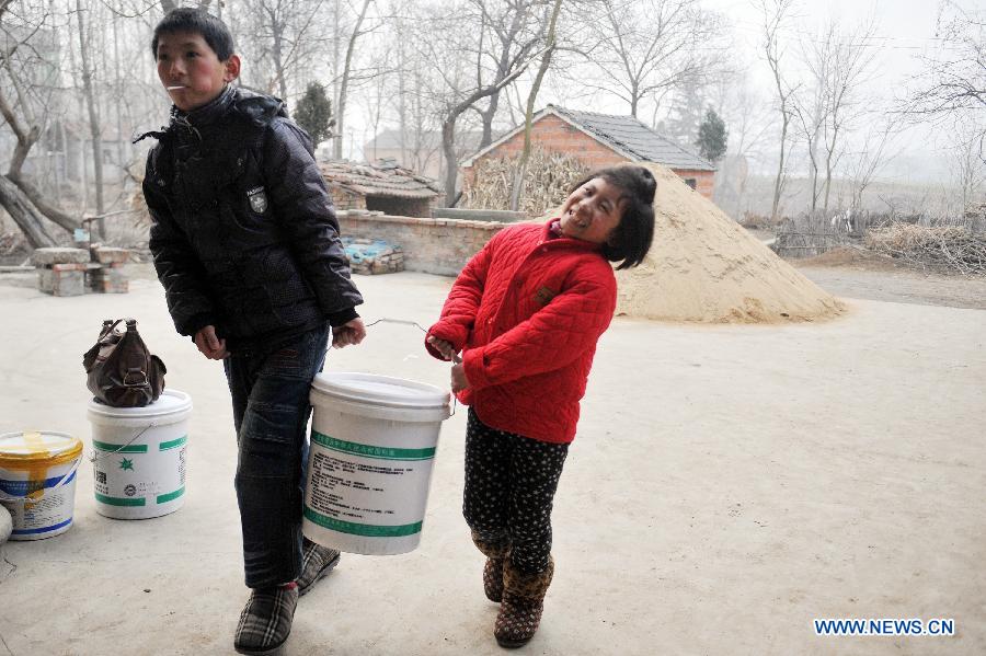 Liu Zhen (L) and Liu Pingping carry a bucket with luggage in their village at Yingzhou District, Fuyang City of east China's Anhui Province, Jan. 29, 2013. (Xinhua/Huang Zongzhi)