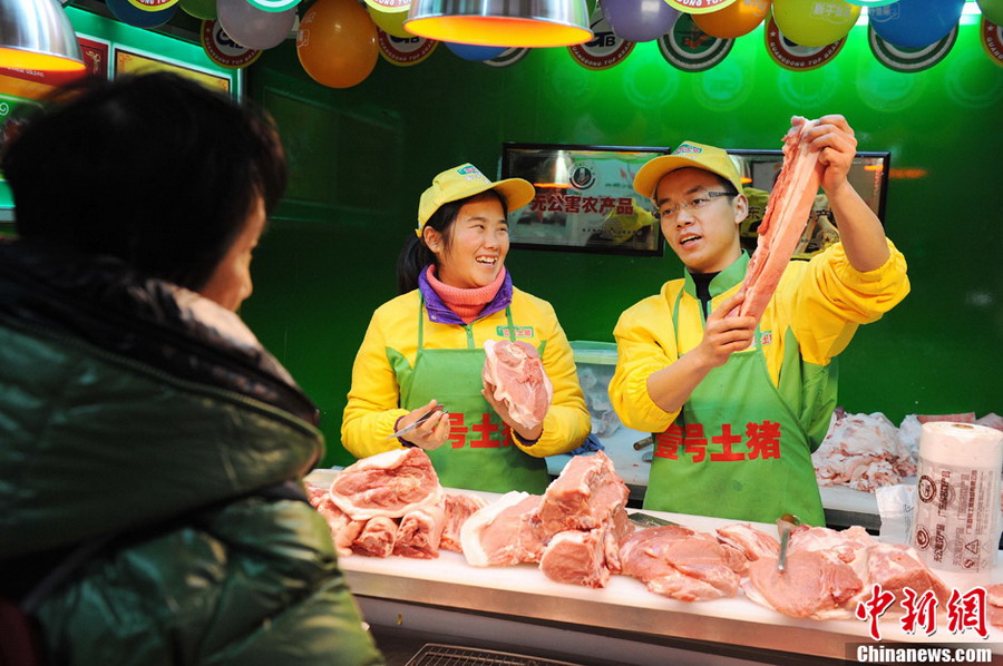 Hao Chengbin (R), a graduate from Jiangxi University of Finance and Economics, and Sun Xia (L), a graduate from University of Hainan, promote pork to a customer at a "No.1 Pork" butcher shop in Shanghai on Jan. 29, 2013. (Photo/CNS)