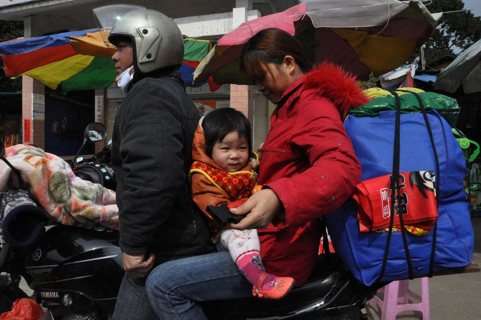 A mother helps daughter to fasten the seat belt on a motorbike after resting at a highway toll station in Fengkai county, south China's Guangdong province, Jan. 30. On Wednesday, about 5,000 motorbikes taking migrant workers home from Guangdong run into the neighboring Guangxi Zhuang Autonomous Region for the upcoming Spring Festival. Traffic police said about 3,000 such bikes passed through the county every day thanks to the well-developed roads connecting Guangxi and Guangdong. Local government offered free services including police escort, food, beverage and medical care to these homecoming people on the motorbike. (Photo/Image China)