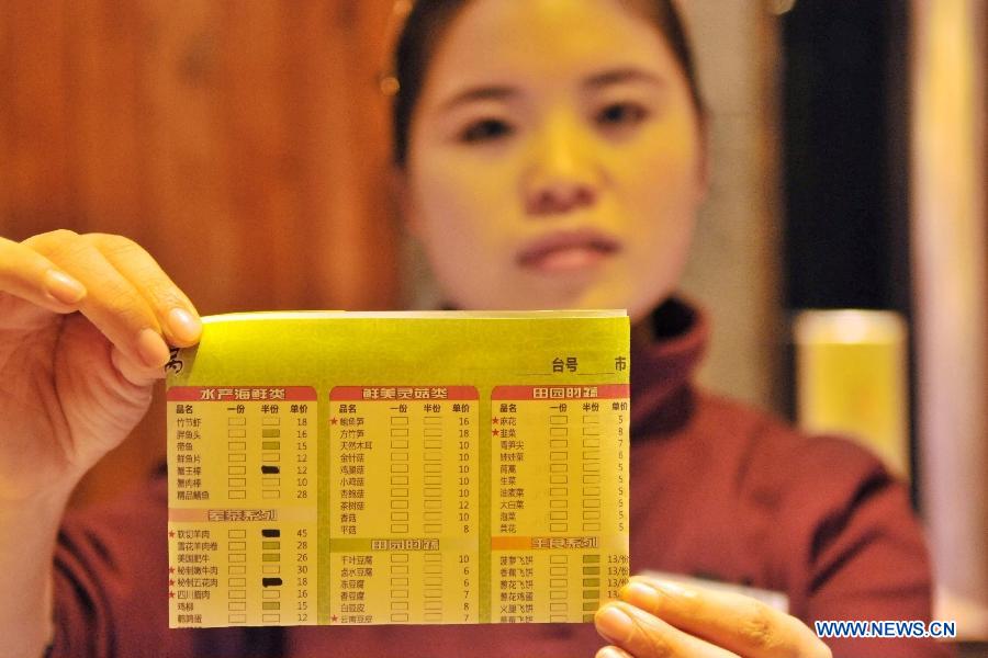 A working staff shows the menu at a hot pot restaurant in Lanzhou, capital of northwest China's Gansu Province, Jan. 30, 2013. A "half portion, half price" activity was launched by numerous hot pot restaurant to advocate saving here Wednesday. (Xinhua/Chen Bin) 