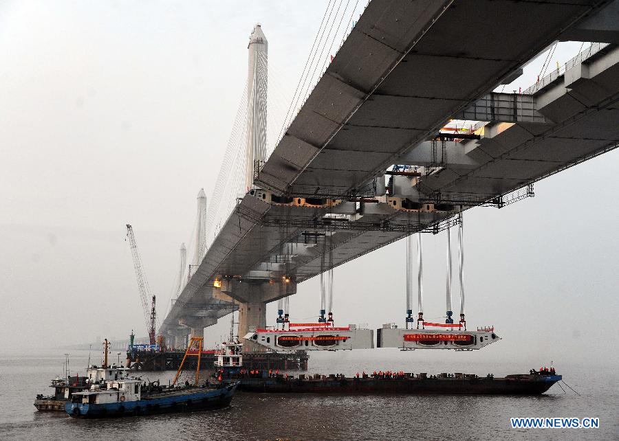 Photo taken on Feb. 3, 2013 shows the last two steel box girders, each of which weighs 408 tons, are lifted up to the floor of the Jiaxing-Shaoxing Sea-Crossing Bridge in Shaoxing, east China's Zhejiang Province. The Jiaxing-Shaoxing Sea-Crossing Bridge, the 2nd sea-crossing bridge in Zhejiang , will be the world's longest and widest multi pylon cable-stayed bridge when it is finished. It is expected to halve the driving time from Shaoxing to Shanghai in east China after putting into use in June of 2013. (Xinhua/Xu Yu)