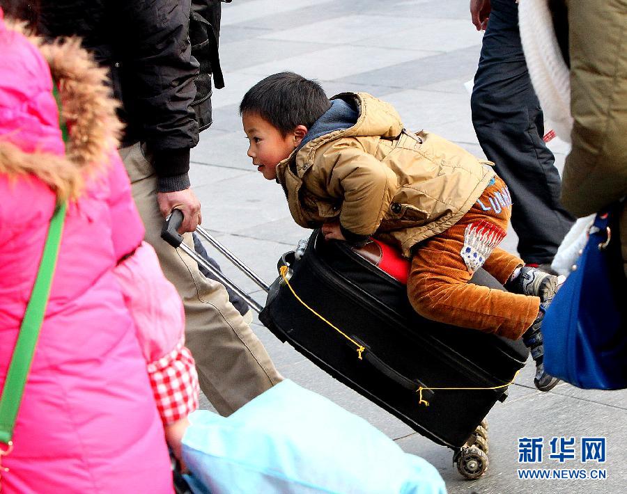 A boy arrives to the Shanghai Railway Station lying on the trolley case of his father on Jan.25, 2013. (Xinhua/Chen Fei)