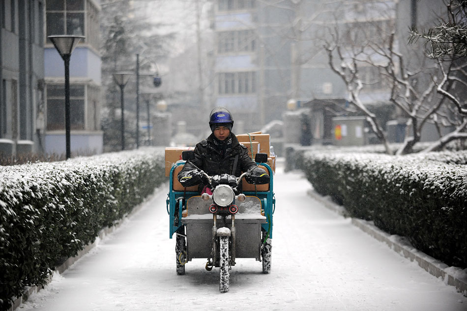 A courier travels through falling light snow in a residential area in Beijing, Feb. 3. (Xinhua/He Junchang)