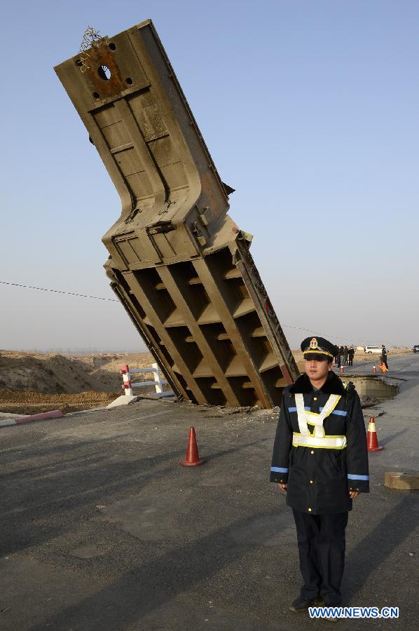 A policeman stand guard beside an outsized casting and its cargo trailer falling down a bridge on No. 304 Provincial Highway, the Shuitao Village, Hongsibao District of Wuzhong City, northwest China's Ningxia Hui Autonomous Region, Feb. 10, 2013. According to local highway authorities, an overloaded truck carrying the outsized casting, with a gross weight of 100 tons, crushed the bridge with design load of only 55 tons when the truck tried to pass over it. (Xinhua/Wang Peng) 