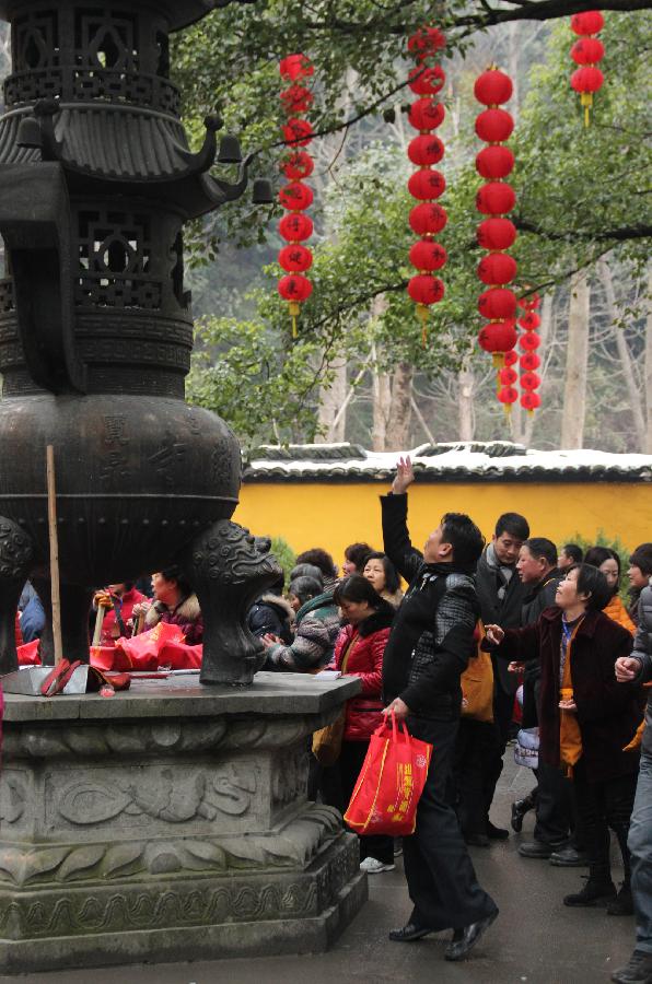 People throw coins into a bronze tripod for blessings in the Faxi Temple in Hangzhou, capital of east China's Zhejiang Province, Feb. 11, 2013. Many people came to the Faxi Temple to burn incense and pray for blessings for the new year on Monday, the second day of the Chinese lunar New Year. (Xinhua/Ma Ping) 