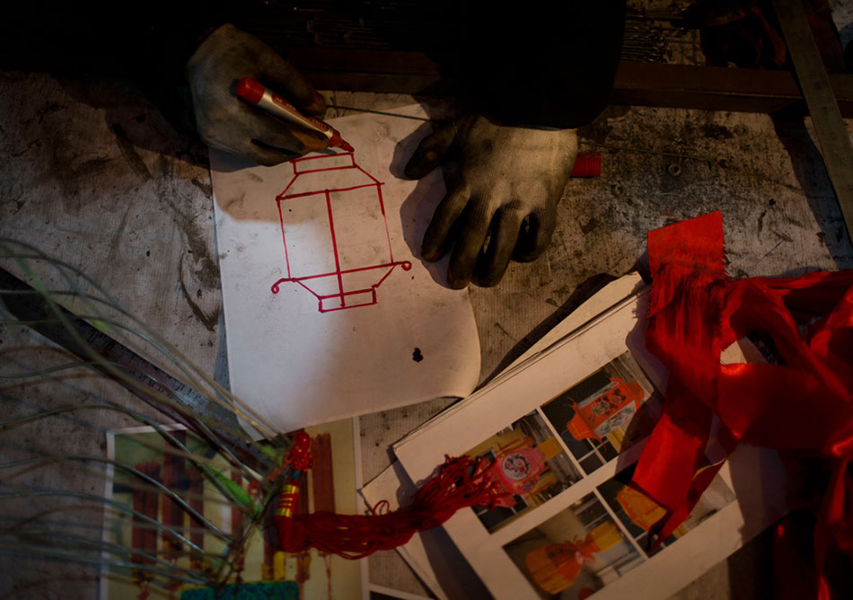 A 58-year-old worker named Liu Shiyou draws the draft of a lantern in the village. Liu's job is to design a lantern according to customers' requirements.