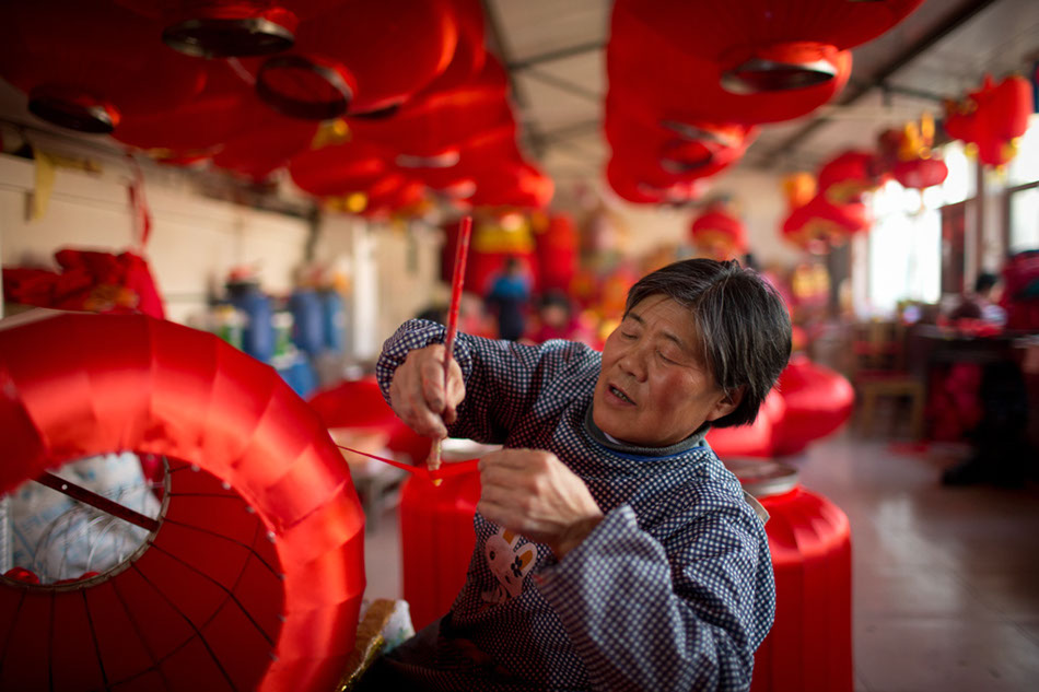 Yan Wanqin, 64, brushes glue on a piece of red silk in Hongmiao village, Beijing's Huairou district, on Jan 26. She is the oldest worker in the village's lantern workshop. [Photos by Kuang Linhua / China Daily]