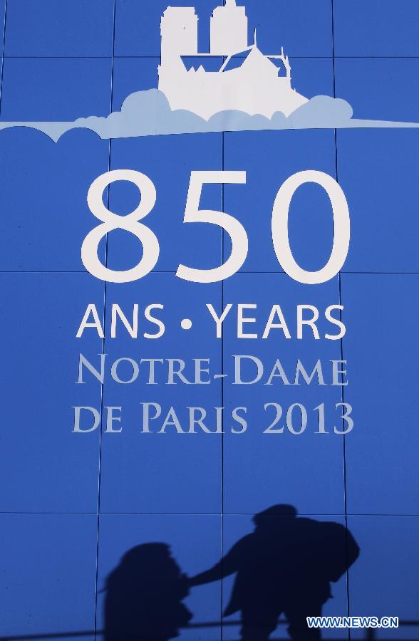 People walk past a poster outside of the Notre Dame de Paris cathedral in Paris, France, Feb. 15, 2013. Notre Dame in Paris will celebrate its 850th anniversary on March 23. Nine new bells will be installed on the cathedral's twin towers to recreate the harmonious chimes before the French Revolution. The new bells are now on display for the public at Notre Dame before ringing on the cathedrale's 850th birthday. (Xinhua/Gao Jing)