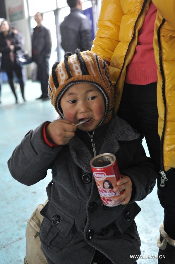 A child eats canned mixed porridge while waiting for the bus at Jinyang bus station in Guiyang, capital of southwest China's Guizhou Province, Feb. 17, 2013. Migrant workers, together with their children, started to return to the urban areas to work after the one-week Spring Festival holiday ended. (Xinhua/Ou Dongqu)