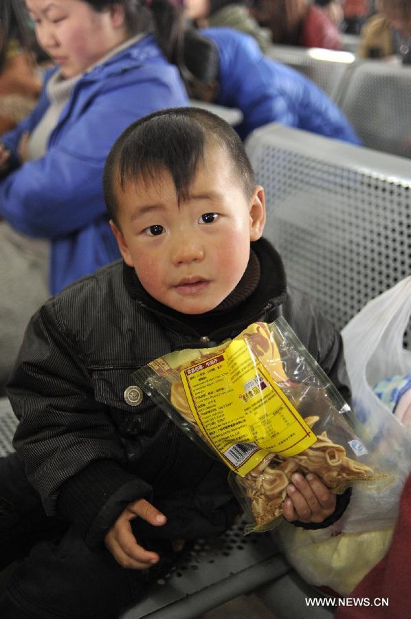 A boy eats snacks while waiting for his bus at Jinyang bus station in Guiyang, capital of southwest China's Guizhou Province, Feb. 17, 2013. Migrant workers, together with their children, started to return to the urban areas to work after the one-week Spring Festival holiday ended. (Xinhua/Ou Dongqu)