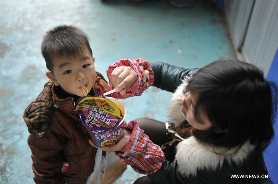 A woman feeds a little boy instant noodles while waiting for their bus at Jinyang bus station in Guiyang, capital of southwest China's Guizhou Province, Feb. 17, 2013. Migrant workers, together with their children, started to return to the urban areas to work after the one-week Spring Festival holiday ended. (Xinhua/Ou Dongqu)