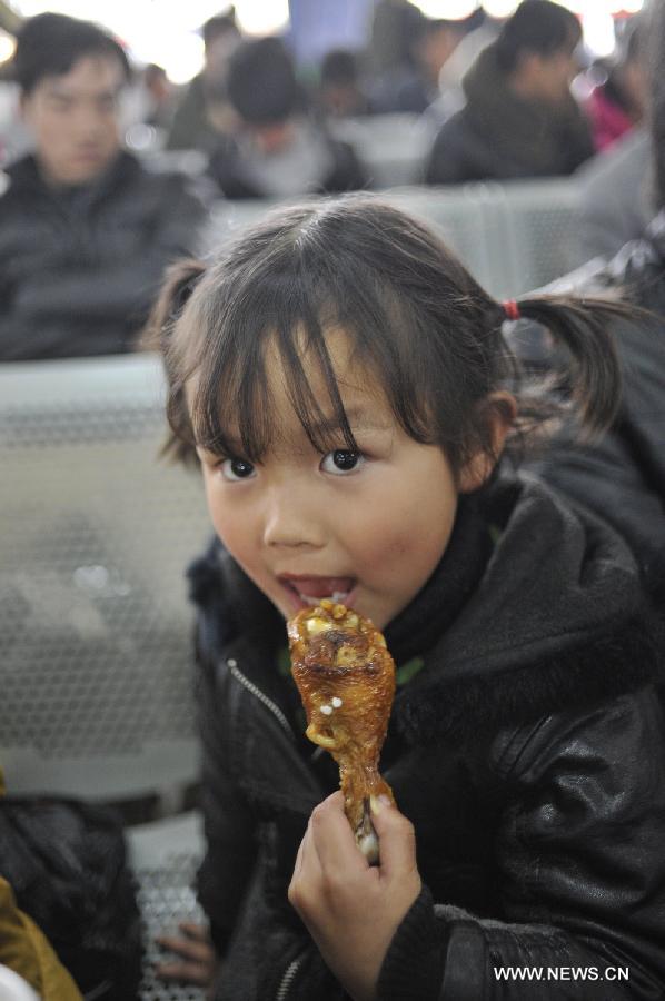 A girl eats a chicken drumstick while waiting for her bus at Jinyang bus station in Guiyang, capital of southwest China's Guizhou Province, Feb. 17, 2013. Migrant workers, together with their children, started to return to the urban areas to work after the one-week Spring Festival holiday ended. (Xinhua/Ou Dongqu)