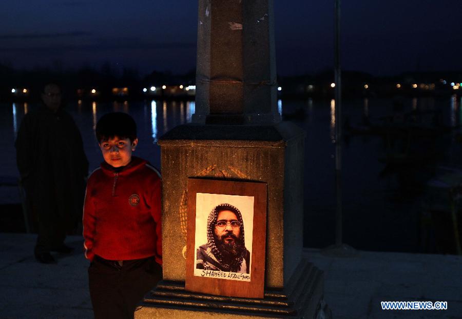 A child stands next to the photograph of 2001 Indian parliament attack convict Mohammed Afzal Guru during a candle light protest demanding Guru's body back in Srinagar, summer capital of Indian-controlled Kashmir, Feb. 17, 2013. (Xinhua/Javed Dar)