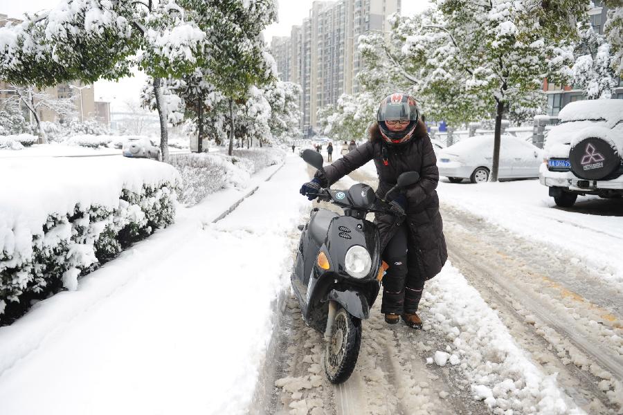 A women walks with her electric bicycle on a snow covered street in Hefei, capital of east China's Anhui Province, Feb. 19, 2013. Snowstorm hit multiple places in Anhui Tuesday morning, disturbing the local traffic. (Xinhua/Du Yu) 