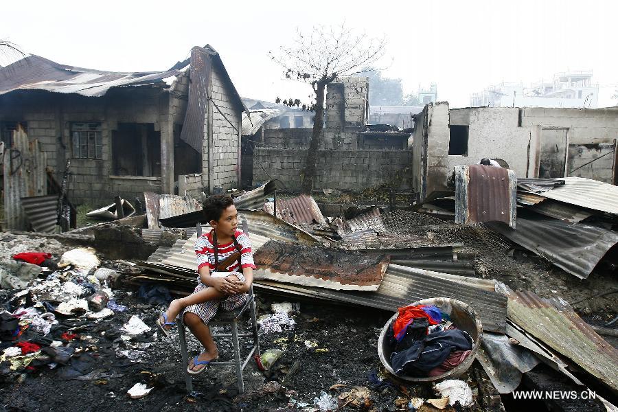 A boy rests after looking for reuseable materials at his charred home after a fire hit a residential area in Valenzuela City, the Philippines, Feb. 19, 2013. Around 500 houses were razed in the fire, leaving 2,000 residents homeless. (Xinhua/Rouelle Umali) 