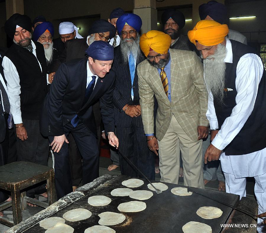 British Prime Minister David Cameron (1st L, front) tries to prepare Chapatti, or flat bread, for a communal vegetarian meal during his visit in Amritsar, India, Feb. 20, 2013. British Prime Minister David Cameron Wednesday paid homage to the victims of the 1919 killing of civilians by British troops in northwest Indian city of Amritsar. (Xinhua/Stringer) 