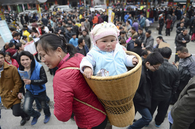 A woman carrying her baby in the back basket looks for job at a job fair in Yiwu, Zhejiang. After Spring Festival holiday, graduates, migrant workers, and a number of job seeker returned to job fairs. 
