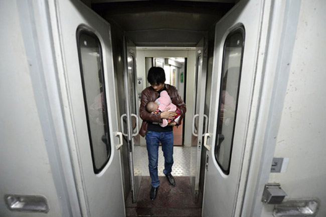 Shi Chunlong pacifies his baby girl to make her fall asleep on a train leaving from Hankou to Hefei on Feb. 15, the last day of Spring Festival holiday. It was the first travel journey of his little girl. (Xinhua/ Zhang Duan)