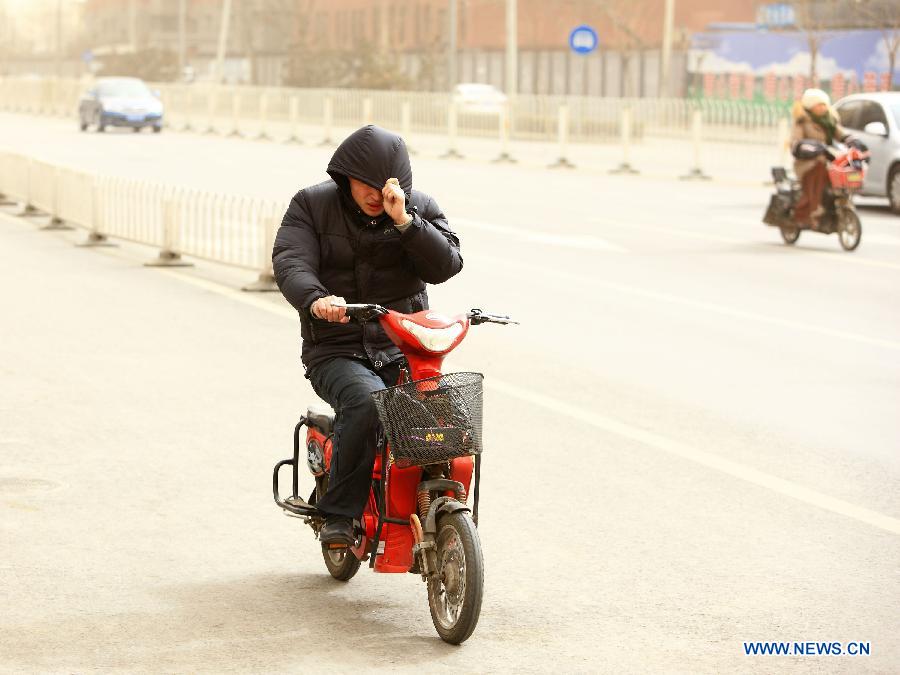 A man rides scooter against strong wind in Beijing, capital of China, Feb. 28, 2013. Beijing was hit by heavy fog on Thursday morning. The fog led to reduced visibility and degenerated air quality. The city also issued high wind and haze alerts on the same day. (Xinhua/Xu Zijian)