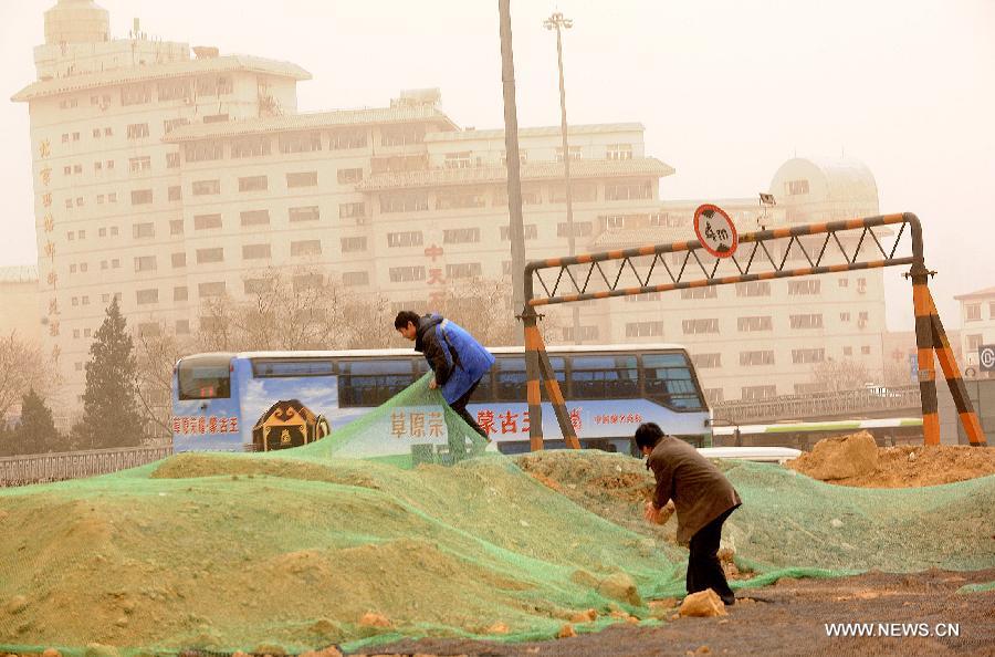 Workers try to cover mound with a net amid dust and sand in Beijing, capital of China, Feb. 28, 2013. A cold front blew away fog and smog which hit Beijing on Feb. 28 morning, but brought dust and sand from Mongolia and north China's Inner Mongolia Autonomous Region. (Xinhua/He Junchang)