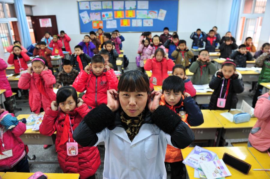 A medical volunteer named Wang Xinrong introduces how to protect ears to the students during an activity celebrating the upcoming Ear-care Day, which falls on March 3 every year, at a primary school in Zigui County, central China's Hubei Province, March 1, 2013. (Xinhua/Wang Huifu)