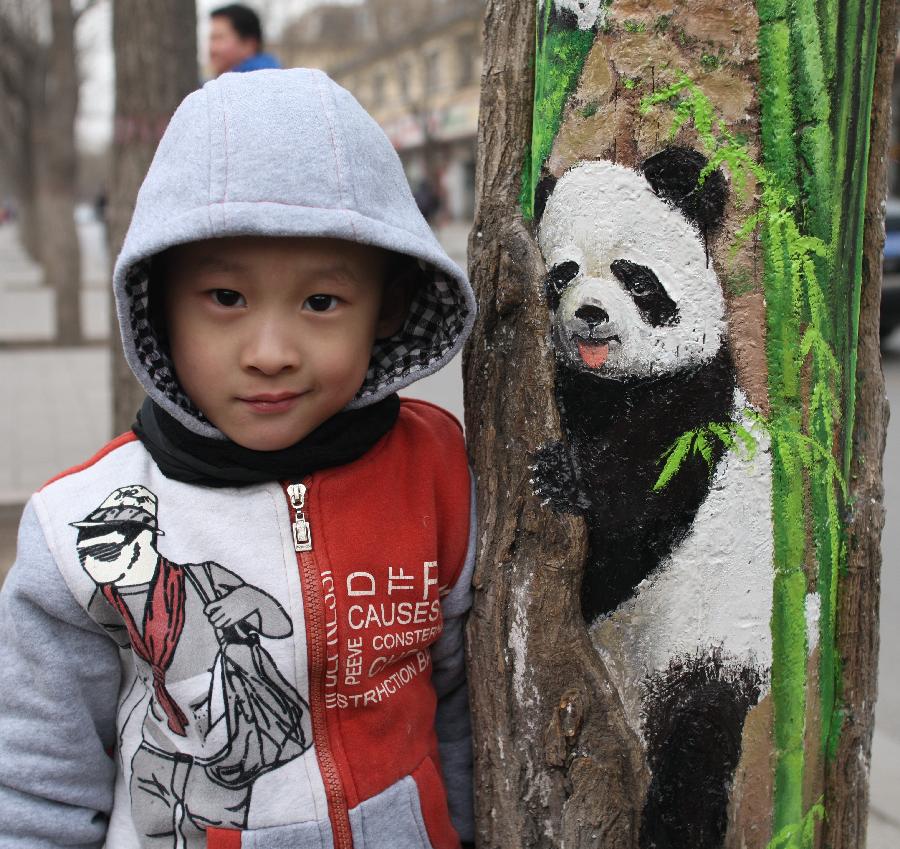 A young boy poses for photo with a tree hollow painting created by Wang Yue, a local college student, at Jiuzhong Street in Shijiazhuang, capital of north China's Hebei Province, March 1, 2013. (Xinhua/Ding Lixin)